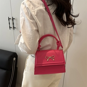 Chic magenta crossbody bag with golden bow and knotted handle in lifestyle setting