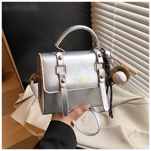 Close-up of metallic silver crossbody bag with baseball charm and yellow fashion text