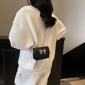 Fashionable black crossbody bag with silver bow accent and chain strap worn by model