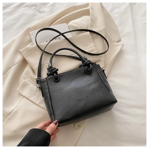 Detail of black lychee grain leather bucket bag with metallic ring knot handle on a blazer
