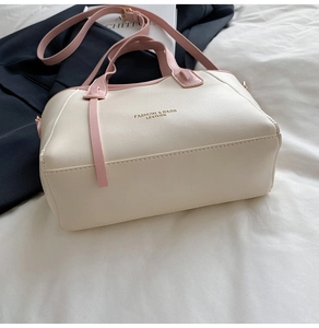 Close-up of beige leather bucket bag with pink handle and gold fashion lettering
