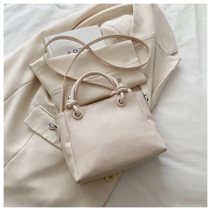 Detail of lychee textured leather tote bag with unique knotted handle design and beige finish