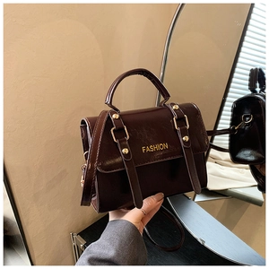 Detail of dark brown glossy handbag featuring golden hardware and fashion lettering