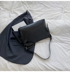 Detail of minimalist black leather tote bag with silver chain strap on white fabric