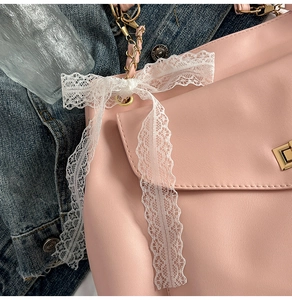 Detail einer rosa Ledertasche mit weißer Spitzenschleife und goldener Kettenriemen