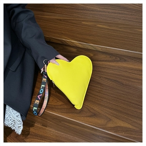 Gelbe herzförmige Lederclutch mit LOVE-Stickerei-Handschlaufe auf einer Holzoberfläche