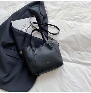 Detailed view of a black leather tote bag with gold hardware on a white fabric surface