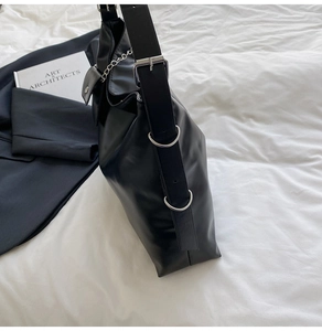 Detail of black tote bag featuring wide adjustable strap with silver buckle and metal chain