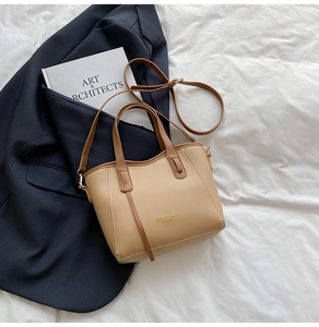 Detail of minimalist leather tote bag with gold logo placed on navy blazer and sheets