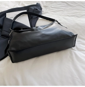 Detail of a minimalist black leather tote bag with glossy finish on a soft fabric backdrop