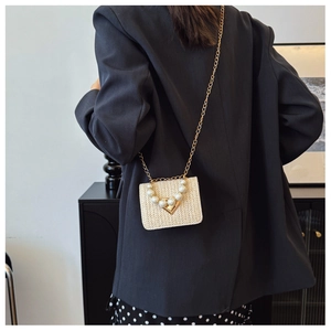 Detail view of woven straw crossbody bag with pearl embellishments on a dark blazer
