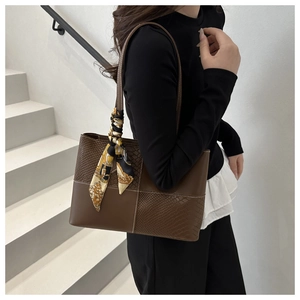 Détail d'un grand sac cabas marron avec texture serpent et anse décorée d'un foulard