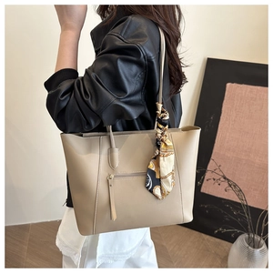 Detail of beige tote bag with a silk scarf tied on the handle and front zipper pocket