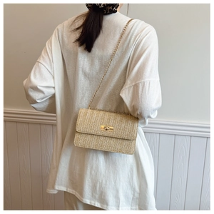 Detail of a straw woven crossbody bag featuring a gold chain strap and metal turn-lock