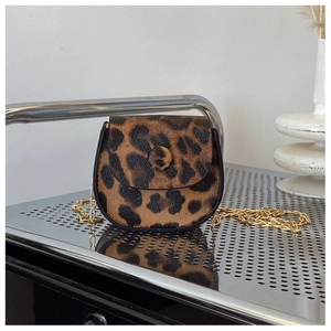 Detail shot of leopard print saddle bag with gold chain strap on a modern metal tray