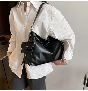 Detail of black faux leather tote bag with silver chain accessory and mini pouch