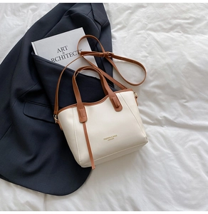 Detail of cream leather tote bag with brown straps and fashion text on white bedding