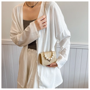 Detail of woven straw mini bag with white pearls and golden triangular buckle closure