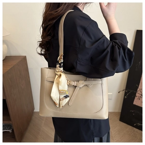 Close-up of a khaki tote bag featuring a decorative leather buckle and silk scarf on handle