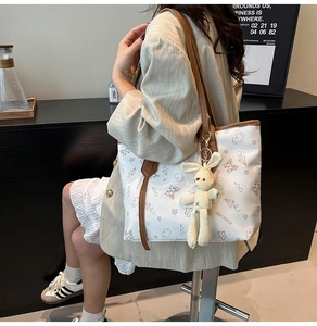 Detail of white tote bag with bear print, brown strap, and plush rabbit pendant