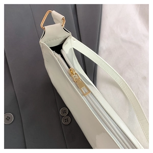 Close-up of white patent leather bag with gold zipper and metallic hardware detail