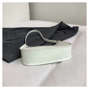 Detailed close-up of glossy white patent leather shoulder bag on a stylish grey suit background