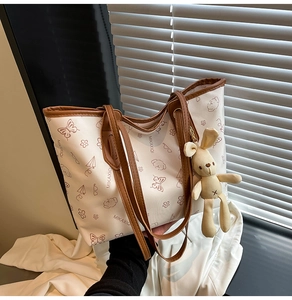Detail view of cream tote bag featuring cute cartoon prints and a rabbit doll charm
