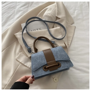 Detail of vintage denim crossbody bag featuring brown leather trim and retro buckle closure