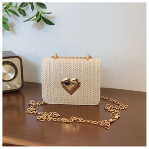 Detail of a straw woven crossbody bag featuring a golden heart-shaped metal lock and chain