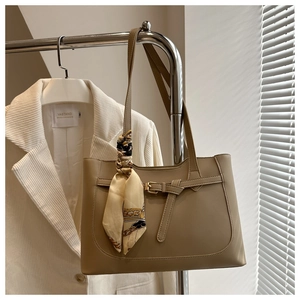 Detail of khaki tote bag featuring metallic buckle belt and elegant silk scarf accessory