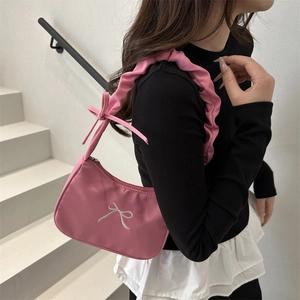 Pink baguette shoulder bag with bow embroidery and ruffled strap worn by a model