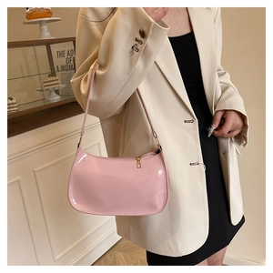 Pink glossy faux leather baguette bag worn over the shoulder with a stylish beige blazer