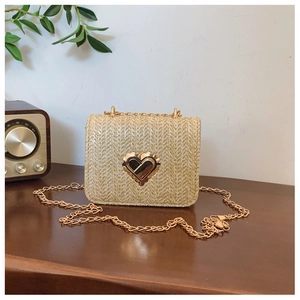 Detail of beige straw woven bag with gold heart clasp and chain on a wooden table