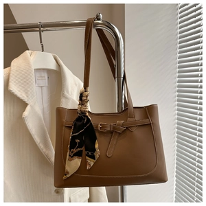 Detail of a brown tote bag with silk scarf accent hung on a metal rack over a blazer