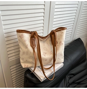 Detail of large tote bag featuring cute floral prints and brown leather handles on a sofa