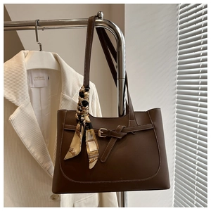 Detail of coffee brown tote bag with decorative buckle and patterned silk scarf on handle