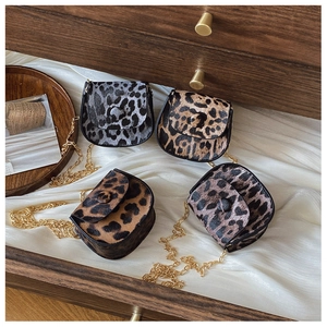 Detail view of four mini leopard print crossbody bags with gold chains on white silk