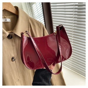 Detailed close-up of dark red patent leather handbag with glossy finish and gold zipper
