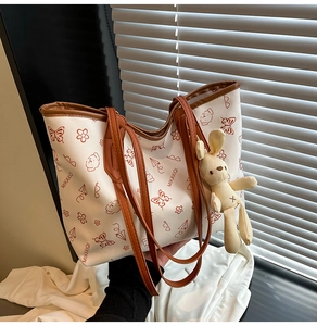 Detail of white tote bag with red-brown prints, leather handles and cute bunny pendant