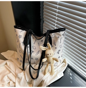 Close-up of white tote bag with black cartoon prints and cute plush rabbit charm