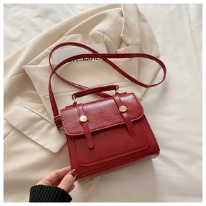 Dettaglio della borsa vintage in pelle rossa con fibbie dorate su una giacca beige