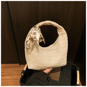 Close-up of beige woven straw tote bag with elegant silk scarf and gold chain handle