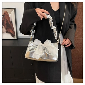 Detail van zilveren handtas met grote witte mesh strik en gouden metalen ketting