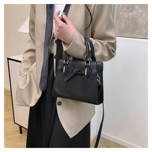 Sac carré noir classique avec nœud décoratif porté par un mannequin dans un cadre épuré