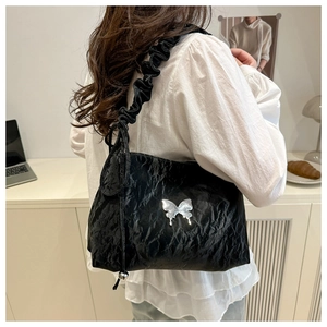 Détail du sac plissé noir avec un papillon en métal argenté et une bandoulière à volants