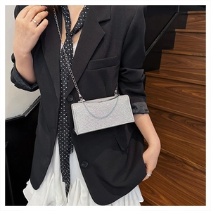 Chic silver sequin clutch bag with metal chain strap held by a model in a suit