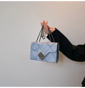 Detailed view of blue denim crossbody bag with golden geometric lock and chain strap