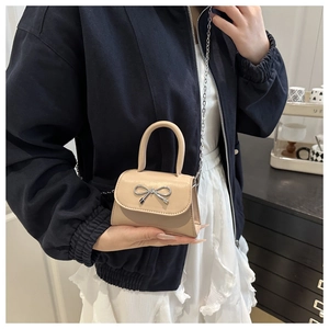 Mini beige leather handbag with silver bow detail and chain strap worn by model