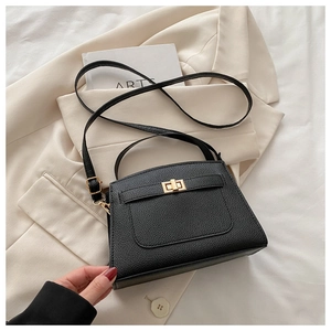 Detail of black lychee grain leather handbag with gold twist lock on beige blazer