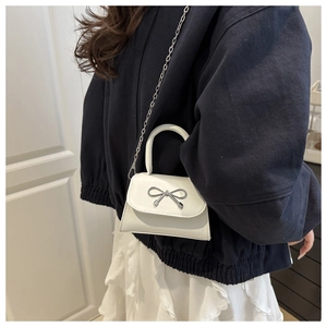 Close-up of a white mini flap bag featuring a silver metal bow and chain strap on a model